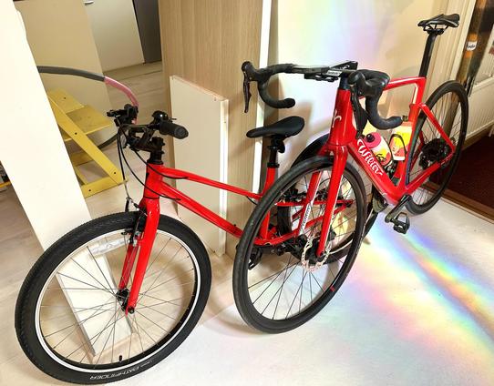 A photograph of two red bicycles side by side. Another one is a kids’ bike from Specialized and the bigger one is a road bike from Wilier.