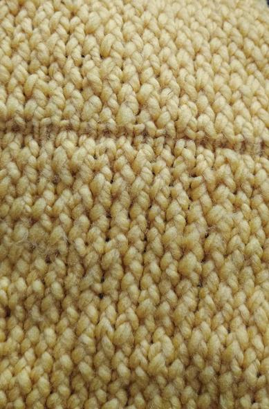Photograph of a loom-knitted work in progress in yellow yarn. Knitted mostly in e wrap stitch with a thin line in another stitch in between.