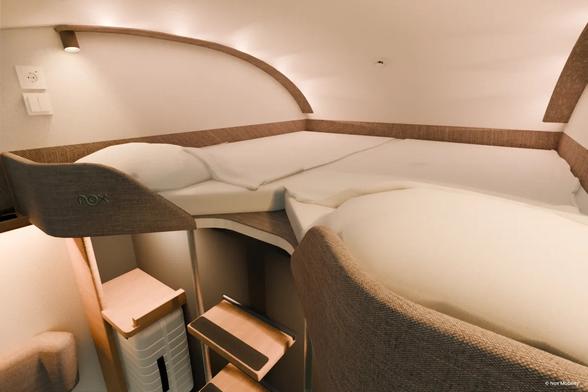 A CG render of the future double-bed train cabin from Nox. Cream white walls with modern wooden furniture, a double white mattress on a mezzanine under the curved roof.
