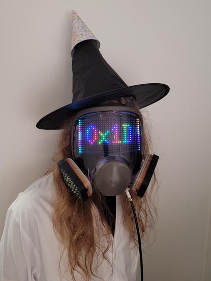 unit ∆-44203 displays 0x1D on its visor in rainbow colors. it is wearing a labcoat and a party hat on the big black witch hat.