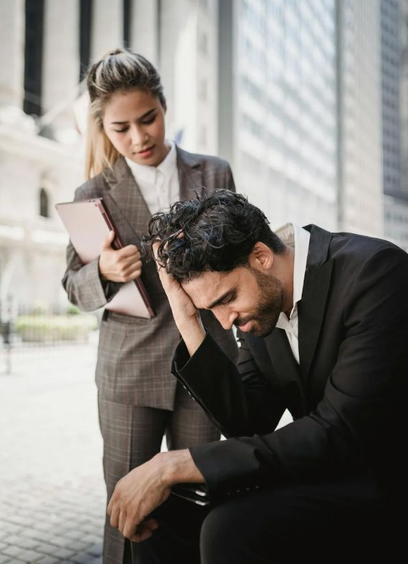 Image of man with hand on head sitting down while young woman in suit looks at him concerned. Image by Ketut Subiyanto via Pexels