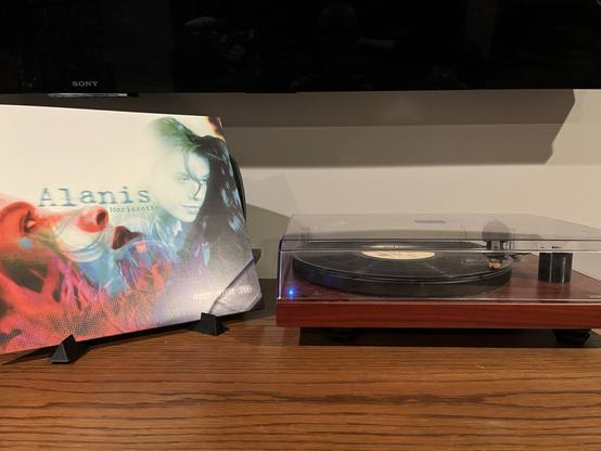 A picture of the album cover for Alanis Morisette's Jagged Little Pill.  It is standing up on the left and features a headshot of Alanis on the right side of the album.  To the right of the album cover, my record player spins a black record.