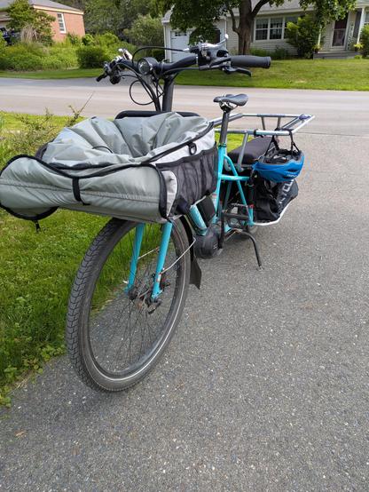 A well used long-tail cargo bike, set up for kid transport. A kids helmet hangs from one of the bars.