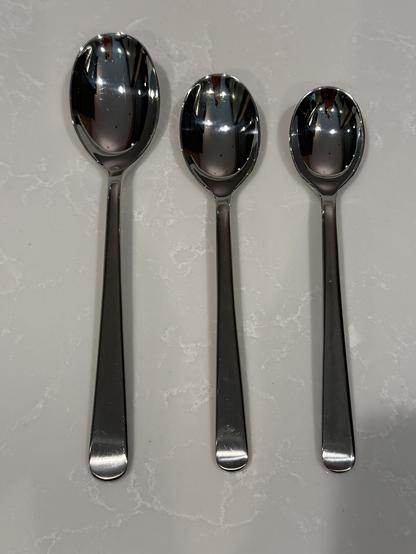 Three shiny metal spoons of varying sizes are neatly arranged on a light marbled surface, reflecting their surroundings.