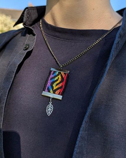 Photo d'un pendentif tissé aux couleurs du drapeau arc-en-ciel porté autour du cou.