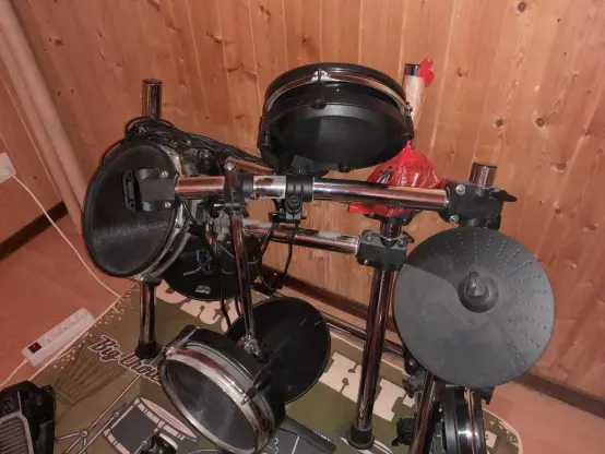 une partie de la batterie électronique repliée sur elle-même. Le tube central du montant fait un arc-de-cercle. Il y en a deux pliés comme ça, du coup c'est impossible de mettre la batterie droite, elle est toute instable et injouable. Y a un sac à caca scotché au montant avec la visserie de la batterie dedans.