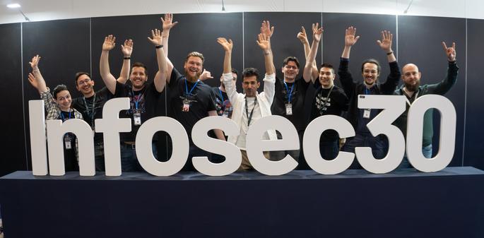 a group of 10 people with their hands up, standing behind a volumetric sign that reads Infosec30