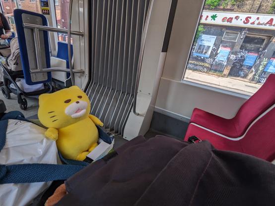 Small yellow cat plush sitting in a bag next to a set of red felt covered chairs, on a Toronto transit streetcar