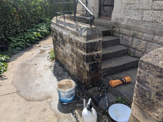 The rear steps of St Catharine's Church, Gloucester. In the foreground, a water sprayer, a bucket of lime mortar, a pointing tool, roll of chisels and dummy hammer. The path is wet from the water spray.