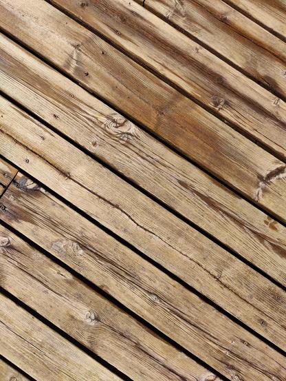 Top-down view of an old, light brown wooden deck. Most of the planks are dry, with a few wet spots.