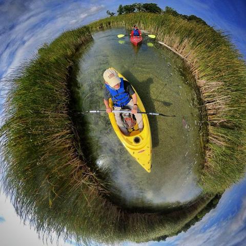 One of a series of photographs in which two people are pictured hiking, biking, and kayaking throughout a beautiful and verdant state park in central Minnesota under cloudy blue late-summer skies.