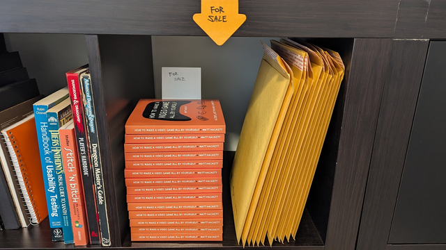 A healthy stack of How to Make a Video Game All By Yourself in an IKEA grid, next to some other books and mailers.