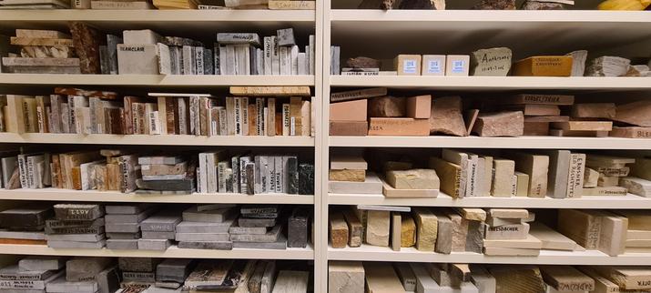 Landscape photo of part of two cabinets with very wide but low plank space filled with stone sample slats. They're mostly sorted by color: various shades of grey, red, brown and yellow and are marked with names like Rose Aurore, Rosso Verona and Bucher Q.Z.
