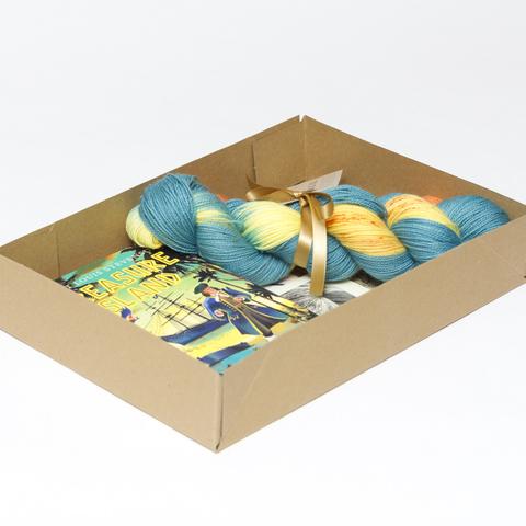 Picture shows an open A4 box containing a sock set of yarn which is blue, yellow and orange and a copy of the Puffin Classic edition of Treasure Island. The rest of the box contents is obscured.