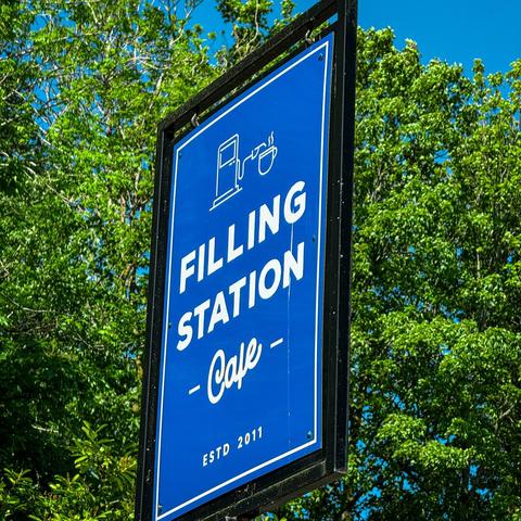 Blue sign with white text that reads “Filling Station Cafe - Established 2011”.