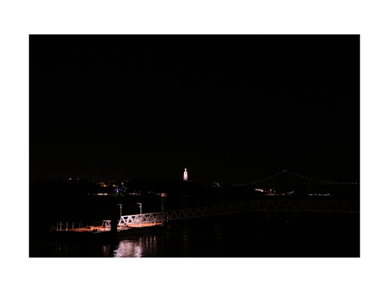 view over tejo river by night with subtle illuminated pier in black water, santuario de cristo rei on left side and ponte de 25 abril bridge in background