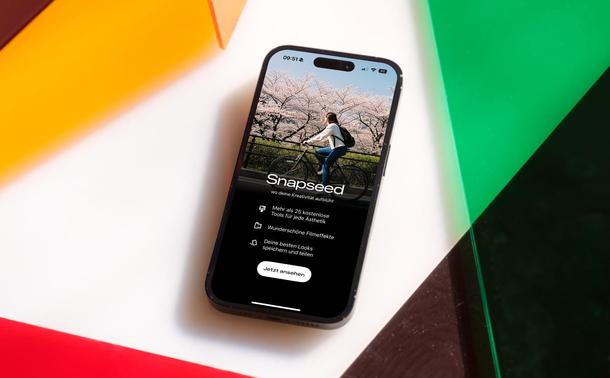 Startscreen von Snapseed in Version 3.0.0 auf einem iPhone, das umgeben von bunten Glasplatten ist.