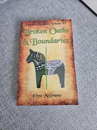 Broken Oaths & Boundaries: Elderkin Chronicles Volume II by Elyse M Grasso
https://books2read.com/BrokenOathsBoundaries

A parchment background with series & author names in Black Chancery and the title in the same font in green

Main image is a green Swedish Dala horse with multicolored decorations, passing through a boundary marked by a green line. The tail end is less distinct and has distorted colors.

Is a walled and locked Residence a palace or a prison? It depends on who holds the keys.

When the Holy Remoran Empire decided that the Emperor’s younger son would marry the heir of the Duke of uncanny Traventi, Childe Silvia saw Leon-Alexander as a fine man and marriage as preferable to war.  

With her Prince dead, Silvia and her 3 young children are trapped at the Emperor’s court far from her homeland, disdained and oppressed by officials who view the Marriage Contract as a cheap tool of conquest while scanting their own promises. The courtiers fear no reprisals for oath-breaking. 

For the Elderkin of Traventi, descended from eldritch creatures, Oaths join the Worlds’ foundations and oath-breaking is no safer than breaking rocks at the base of a cliff, inviting cosmic rupture.

The warnings of Silvia’s younger son, the Notary and seer Franz-Karl, become more urgent as Contract breakage and other villainy continues unmended and news of disaster spreads. 

Will reforms avert the looming calamity? Or will it all end in tears?