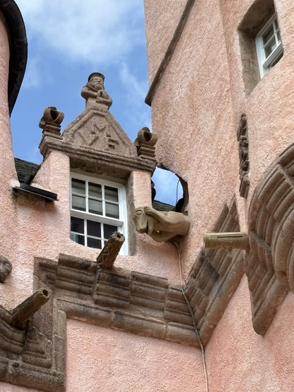 A gargoyle covering its ears juts out near a window close to the roof line. Odd looking beast.