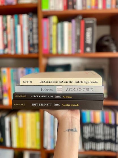 A hand holding a pile of books in front of a book shelf