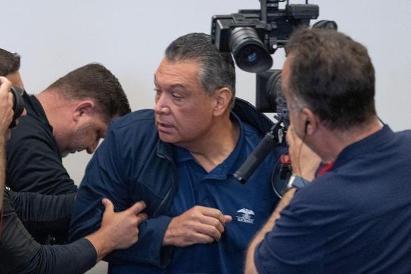 Senator Padilla is in the midst of being dragged out of the room of Secretary noem's press conference, surrounded by are presumed to be federal agents. Senator Padilla's polo shirt has an American Eagle logo type graphic on it and the words "U.S. Senate" clearly visible.