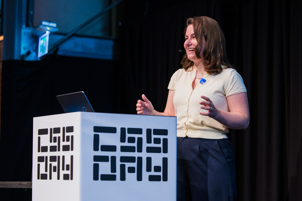 Cyd smiling and speaking behind a lectern saying “CSS day” gesturing with her hands