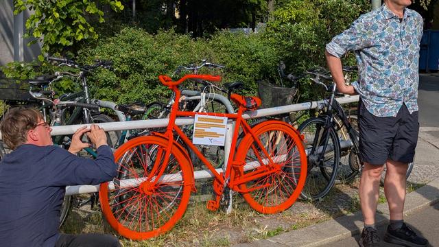 Ein knallrotes Fahrrad mit einem laminierten Plakat steht an einem Geländer.