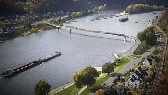 Eine geschwungene maximal Fußgänger- und Fahrradbrücke überspannt den Rhein, auf dem Frachtschiffe fahren. Grüne Ufer, eine nahe Bahnstrecke und kleine Häuser prägen die ländliche Szenerie.