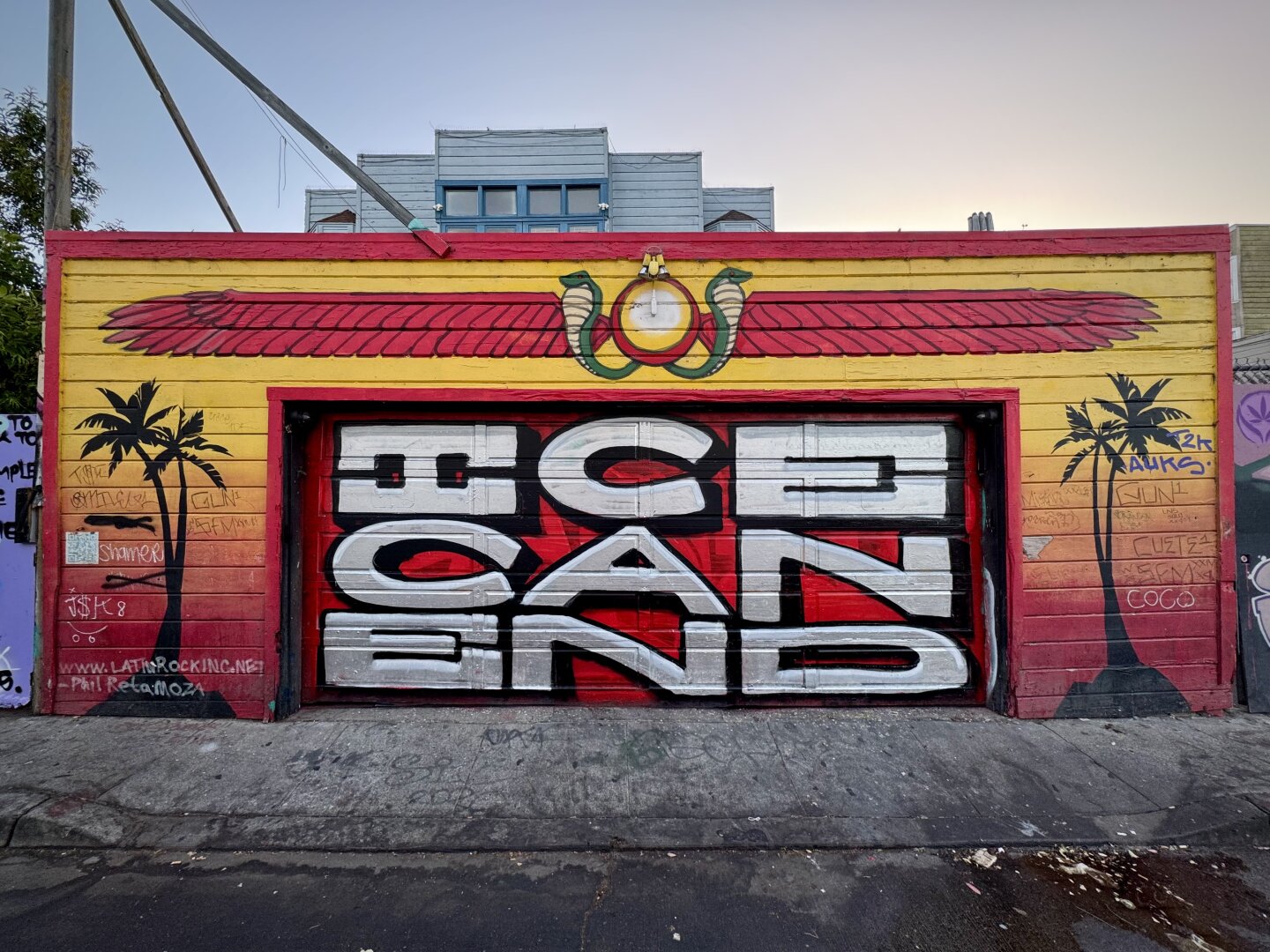 Large graffiti on a wall in San Francisco. The text has three words, Ice, Can, and End, written in a 3 by 3 square. So the words can be read from left to right, or from top to bottom. This graffiti is painted on a double wide garage door in Osage Alley. On the wall above and around the garage door is another mural that looks like it was inspired by Mayan buildings and ornamentiation.