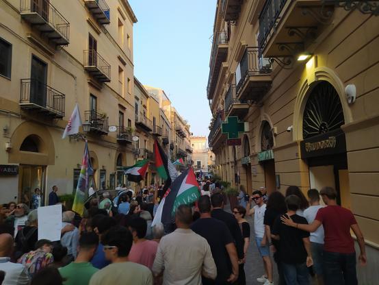 Persone di spalle in Via Atenea ad Agrigento con diverse bandiere della Palestina