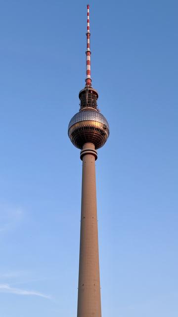 The image features the Berlin TV Tower, a tall structure with a spherical observation deck at the top, set against a clear blue sky. The tower is characterized by its cylindrical shape and red and white antenna.