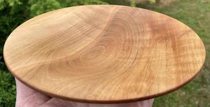 A wooden plate held on fingertips. The wood has distinctive grain and stress patterns.