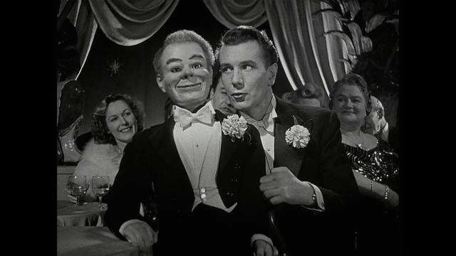 still from Dead of Night, a 1945 film, showing a male ventriloquist and his dummy in evening dress, performing in a club