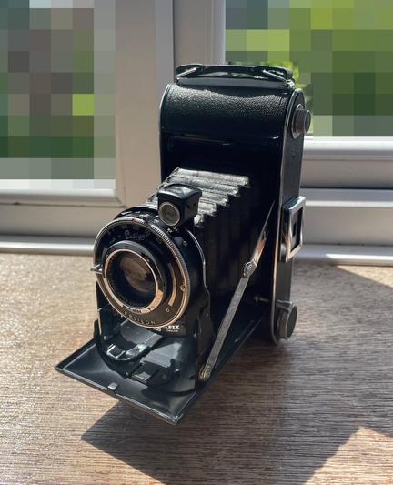 photo of a gorgeous vintage folding camera; bellows protrude from the body with a lens assembly mounted on the front