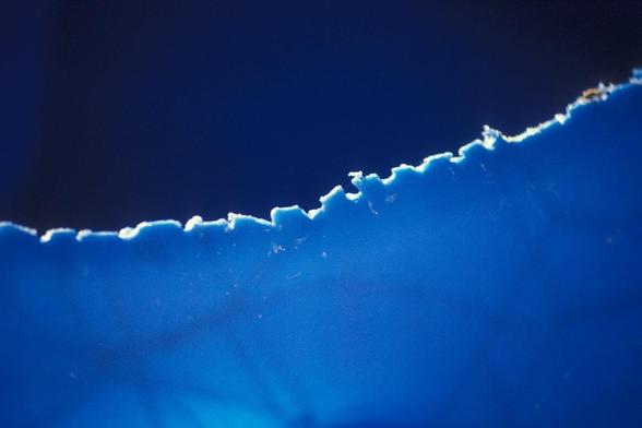 Close-up of a jagged, illuminated edge on a blue surface against a dark background.