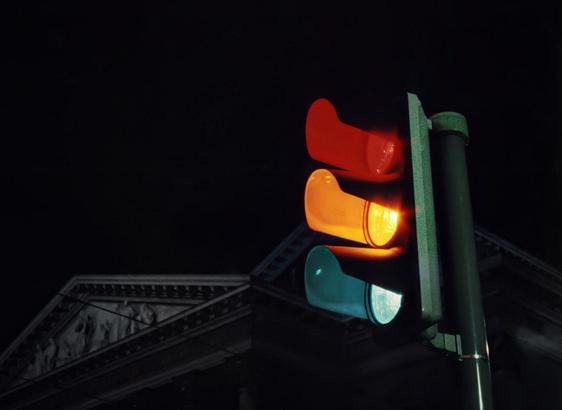 Traffic light against a dark sky with red and yellow lights illuminated. A classical building with ornate detailing is partially visible in the background.