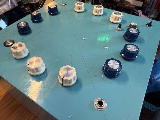 The top of a large, square box colored sky blue and adorned with a circle of dark blue and white knobs. In the corners are a few switches and jacks.
