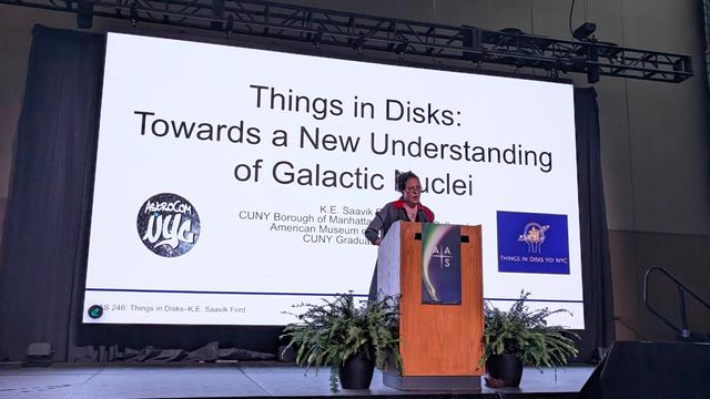 Saavik Ford stands on stage behind a podium. Behind her is a giant screen with slides: Things in Disks: Towards a New Understanding of Galactic Nuclei, K.E. Saavik Ford.