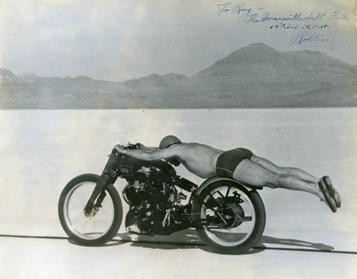 A picture of a man riding a motorcycle on the Bonneville salt flats. He is wearing only swim trunks and shoes. He is laying on the motorcycle with his legs and feet straight out past the rear tire. 

It is Rollie Free setting a speed record in 1948.