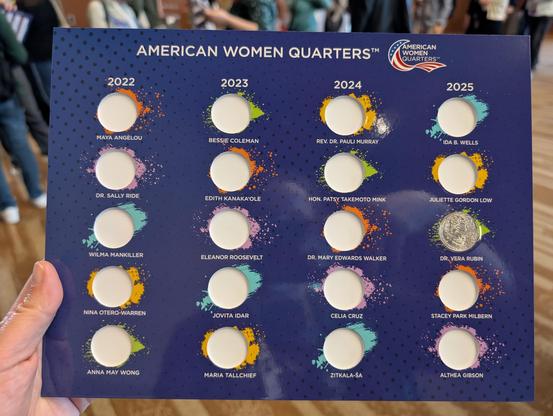 A cardboard display with a grid for holding the American Women Quarters. They are all empty except for Dr. Vera Rubin.