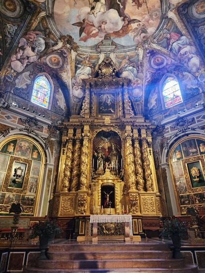 At center, altar and large altarpiece; the latter is about 25ft tall, has three Rococo columns on each side with two statues inset in the center, and is painted entirely in gold. Surrounding these are the Rococo molding and frescoes typical of this church.