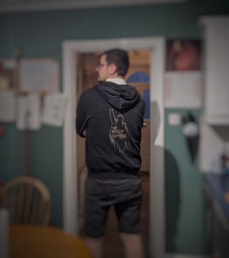 A photo of the back of a man wearing a black hooded sweatshirt. The hoody has the artwork from Rage Against the Machine's Battle of Los Angeles album, bleach dyed on to the back of it.