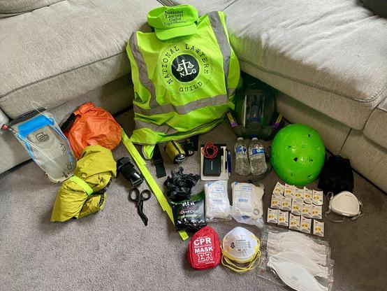A pile of items, including an NLG Legal Observer vest and hat, safety gear including a respirator, and gear to survive gunshot wounds.