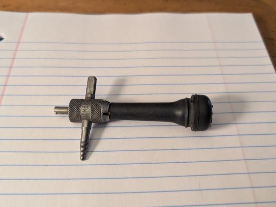 A valve core service tool, on the end of a valve stem. They're laying on a piece of notebook paper.