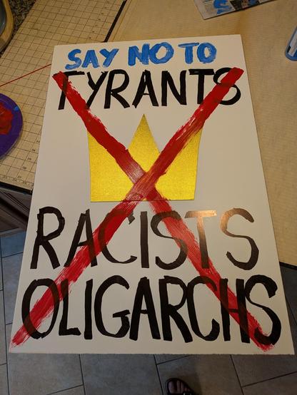 A poster with a cut-out gold crown in the center. It says "Say no to tyrants, racists, oligarchs" around the crown. A big red painted X crosses out all the bad things to get rid of.