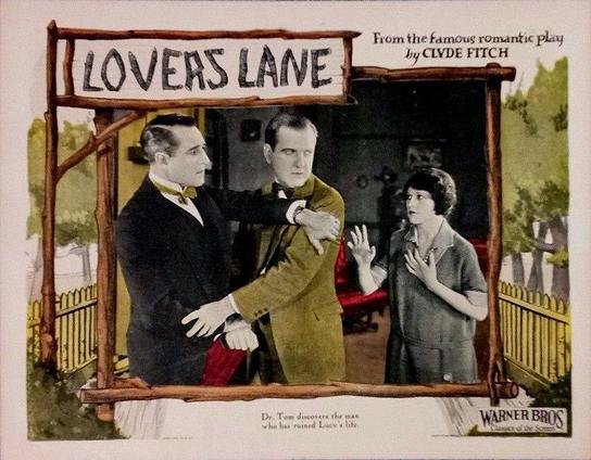 Lobby card of the film. Two men are apparently about to start fighting while a woman close to them try to prevent it. One of men is wearing a black suit, the other man is wearing a brown suit. The woman is wearing a short-sleeved gray suit.