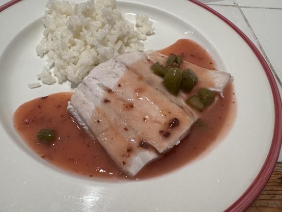 Pink and white plate with pink and white fish, sauce and rice.