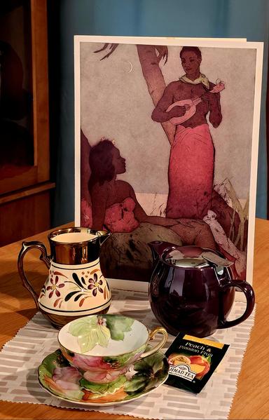 Tea tableau in muted spice colors with a backdrop of 1951 artwork depicting a native Hawaiian man serenading a young Hawaiian woman with an ukulele. There is a tropical looking vintage cup and saucer set, a 1930s creamer, a deep purple teapot, and Peach Passionfruit black tea from Ahmad.