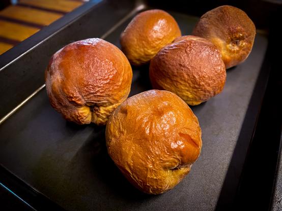 Quinces, a little browned and with wrinkled skin after being roasted, sit in a baking pan cooling.