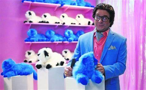 Hombre con traje azul frente a estantes con peluches en forma de animales, sosteniendo un peluche azul en una escena de la película 'La fiebre de los peluches Beanie'.